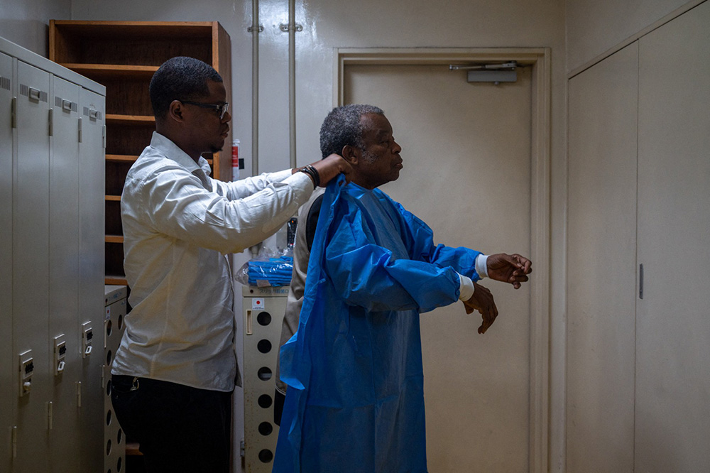 A worker (L) helps Professor Jean-Jacques Muyembe, director general of the National Institute for Biomedical Research (INRB), to put on protective equipment before entering a laboratory in Kinshasa, Democratic Republic of the Congo, on May 20, 2026. (Photo by Hardy BOPE / AFP)