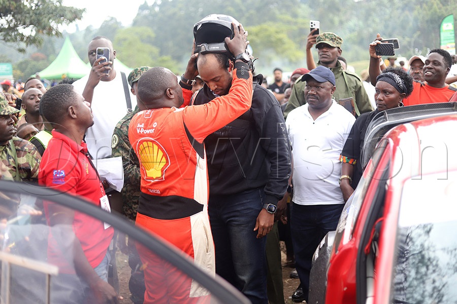 Ronald Ssebuguzi's navigator, Anthony Mugambwa, helps King Oyo put on his helmet before a drive with Ssebuguzi during the UMC Fort Portal Rally. Photo: Johnson Were