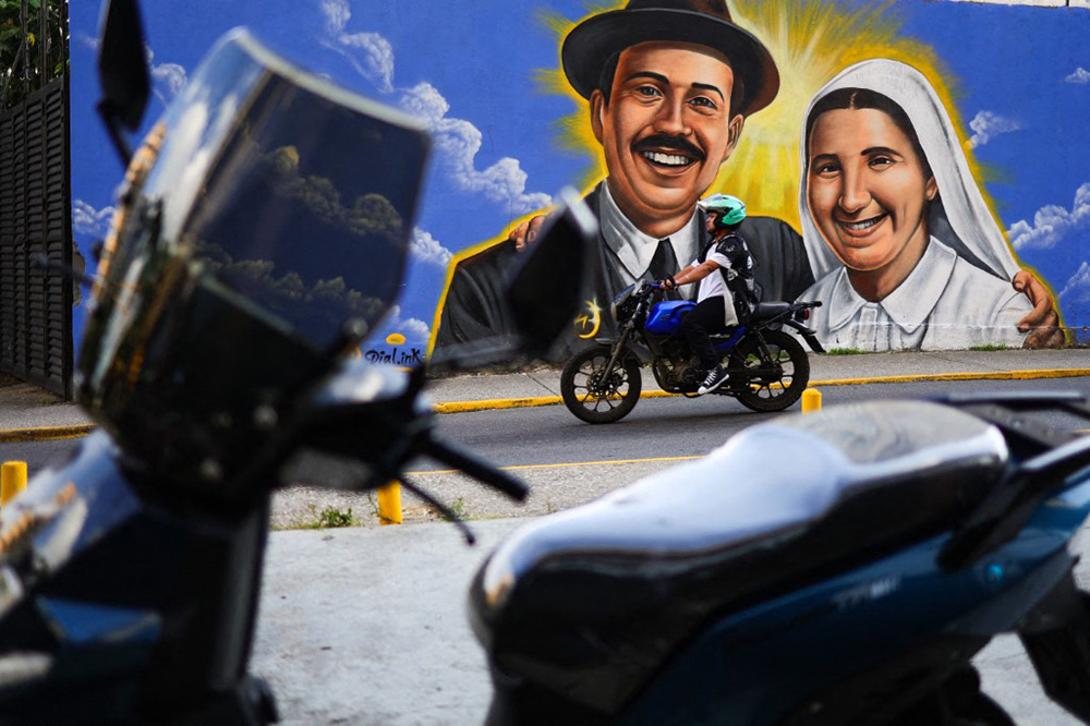 A motorcyclist passes in front of a mural of Dr. Jose Gregorio Hernandez and Sister Maria del Carmen Rendiles in Caracas, Venezuela, on October 18, 2025. (Photo by Javier Campos/NurPhoto) (Photo by Javier Campos / NurPhoto via AFP)