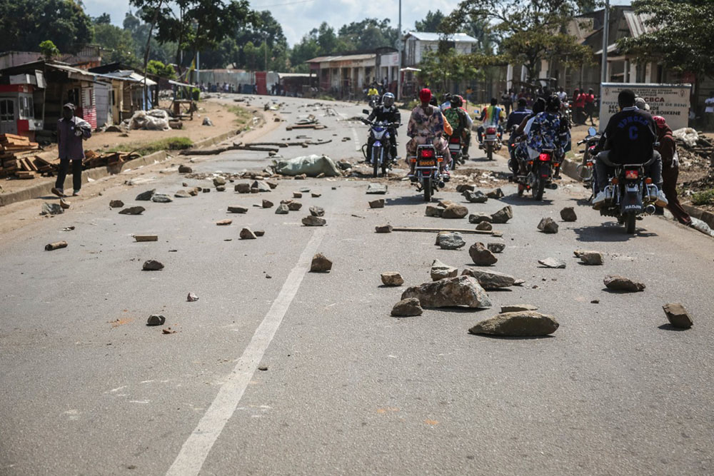 Motorcyclists ride past stones blocking a road following an attack attributed to the Allied Democratic Forces (ADF) in Beni, North Kivu province, eastern Democratic Republic of Congo, on May 31, 2026. (Credit: AFP)