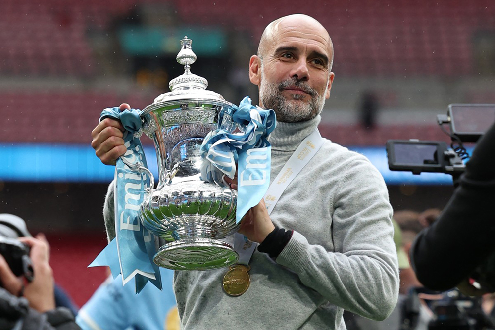 Manchester City's Spanish manager Pep Guardiola poses with the trophy on the pitch after the English FA Cup final football match between Chelsea and Manchester City at Wembley stadium in London, on May 16, 2026.