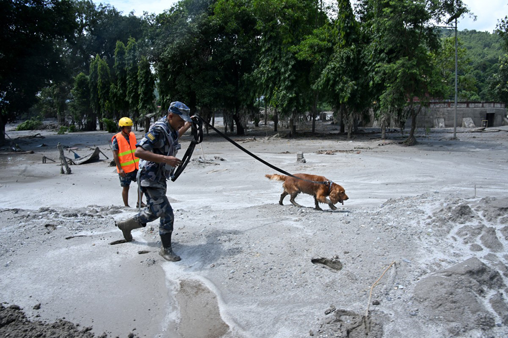 A member of the security forces and his sniffer dog search for survivors following flash floods at Trishuli in Nepal's Nuwakot district on August 27, 2026.