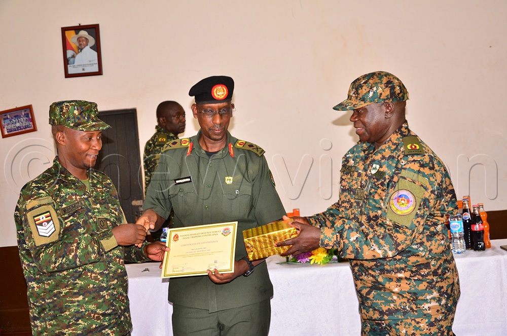Sgt. Abel Muhumuza (L) receives a certificate of completion from Munanura, as the TLC commandant, Maj. Sam Waako (R), holds his gift for the overall best student at Gaddafi Barracks in Jinja on Friday. (Photo by Jackie Nambogga)