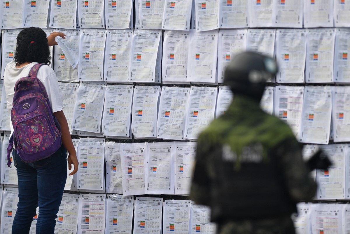 A member of the Military POlice of Public Order (PMOP) stands guard as a woman looks at the "victory wall" of Tegucigalpa's Mayor and candidate for re-election, Jorge Aldana, outside the Electoral Logistics Centre, located at the National Institute for Professional Training (INFOP), where the count of ballots with inconsistencies in Tegucigalpa is taking place on December 19, 2025. (AFP)