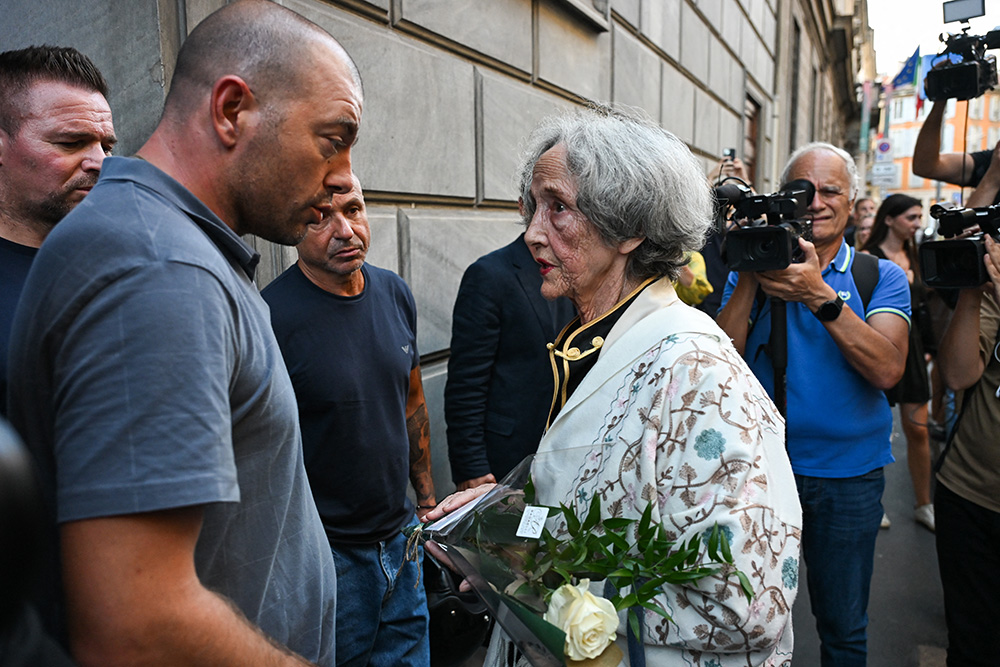 A woman gives flowers with a card reading ‘Dear Giorgio’ to a security guard outside the headquarters of Italian Fashion House Giorgio Armani after the announcement of the death of it's founder Giorgio Armani, in Milan on September 4, 2025. (Photo by Piero CRUCIATTI / AFP)