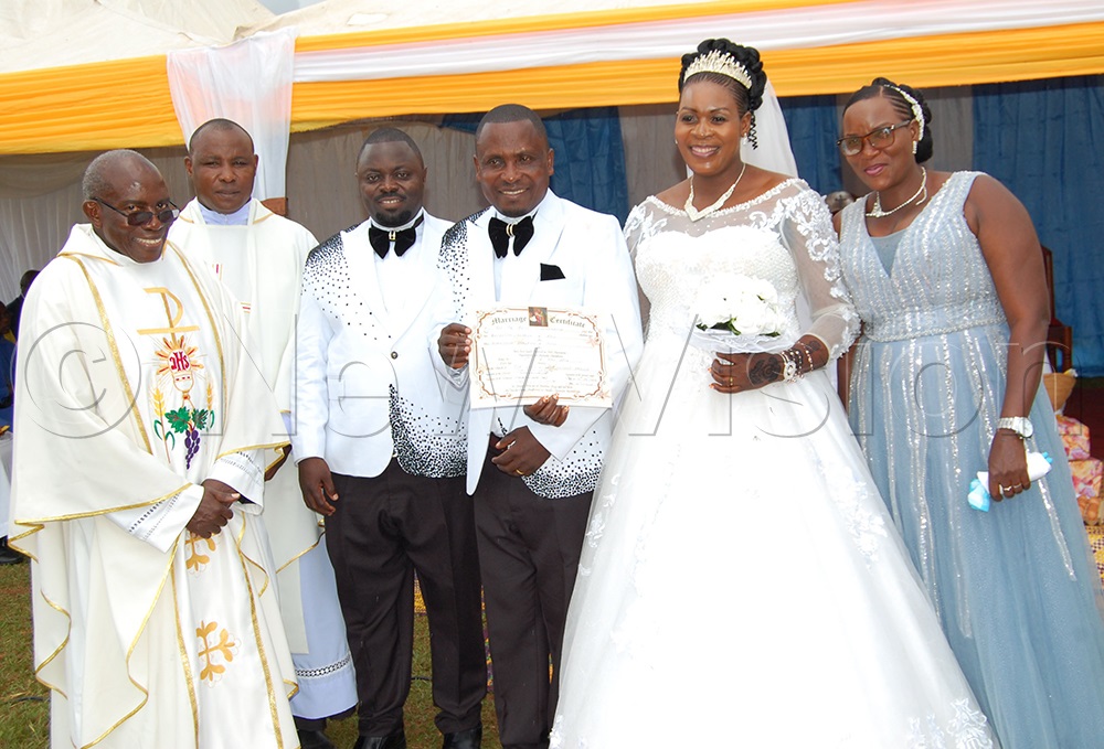 Msgr. Charles Kasibante (left) shares a photo moment with the couple he wedded. (Photo by Mathias Mazinga)