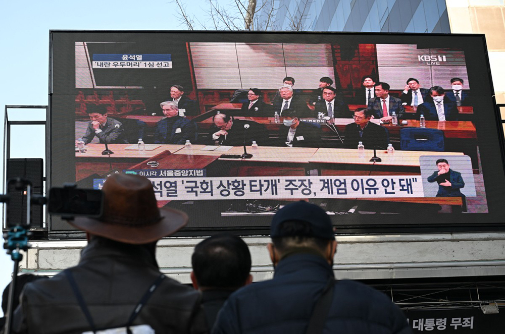 Supporters of South Korea's impeached former president Yoon Suk Yeol watch a live stream of Yoon's trial on his insurrection charges near the Seoul Central District Court in Seoul on February 19, 2026, as Yoon (2nd row L) is seen on the screen.  (AFP)