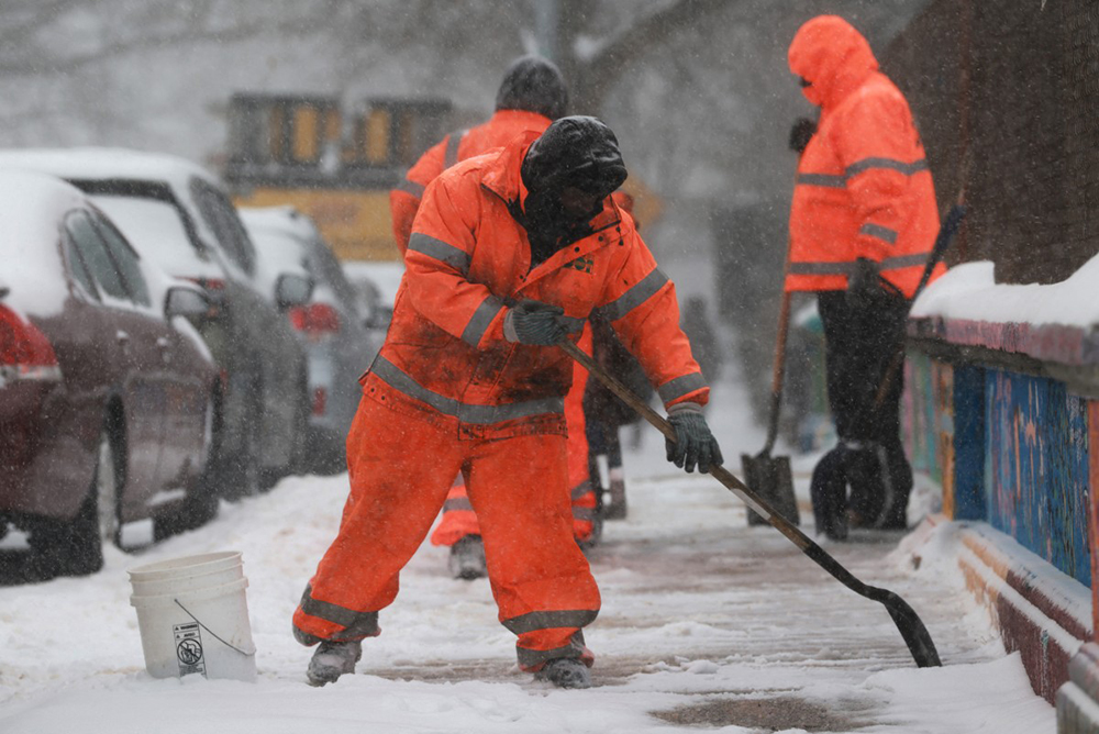 City workers clear a sidewalk of snow in Brooklyn as a major winter storm moves through the area on January 25, 2026 in New York City.