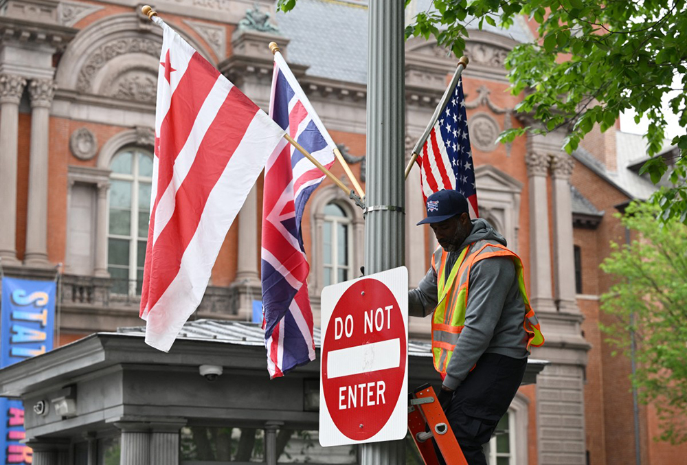 A worker puts up flags on a lamppost near the White House ahead of a visit by Britain's King Charles III, in Washington, DC on April 25, 2026. 