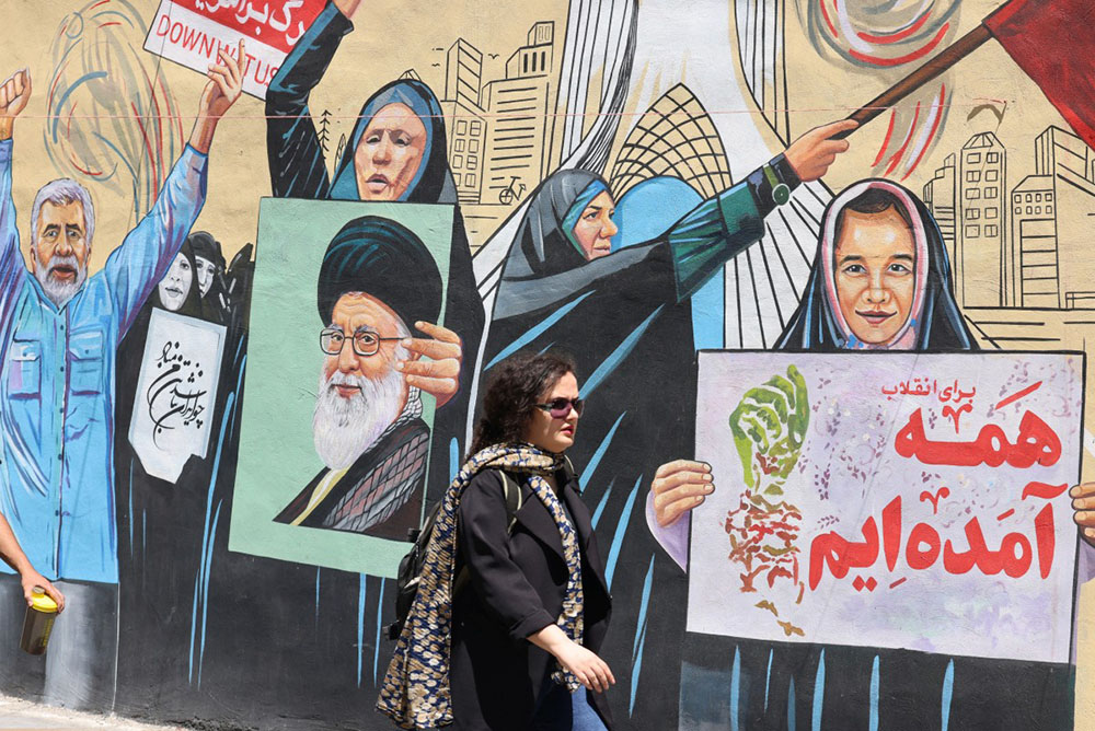 An Iranian woman walks past an anti-US and anti-Israel mural painted on a wall, in the capital Tehran on May 10, 2026. (Credit: AFP)