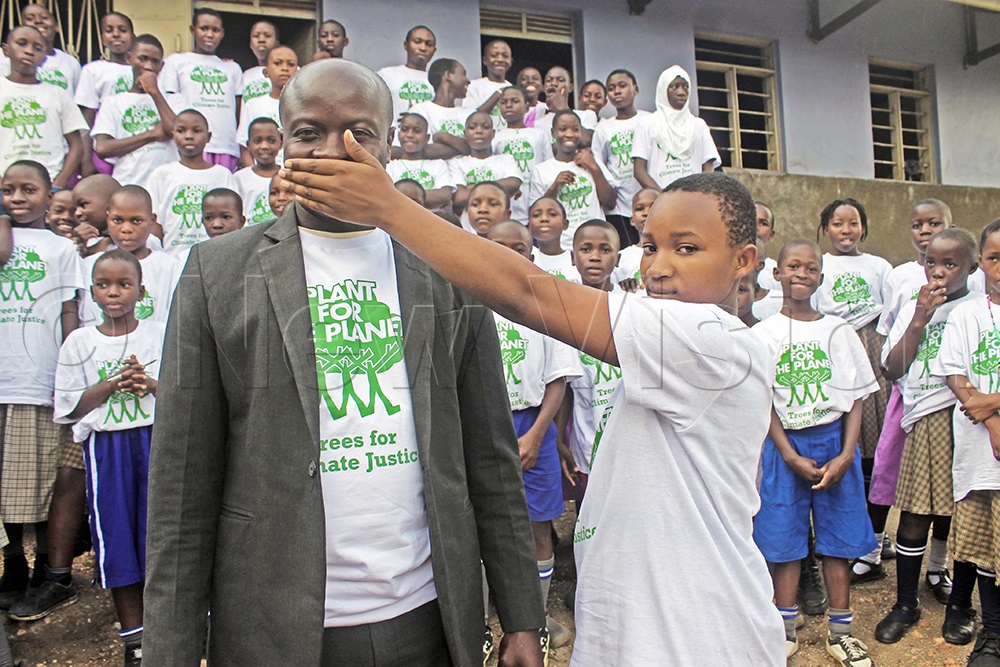 One of the pupils making a gesture with Chief guest, Joseph Isingoma, the Kasese district disaster focal person, demonstrating to the general public to stop speaking, but rather plant trees. (Credit: Samuel Amanyire)