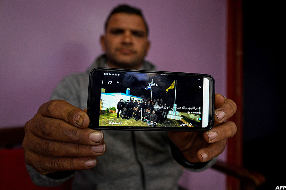 A man holds a phone showing a picture on a social media network believed to include some of his relatives before they reportedly went missing in the Mediterranean Sea while making the journey to Europe through Libya.