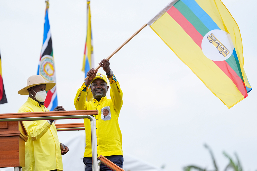 Deputy Speaker of Parliament, Thomas Tayebwa waving the NRM flag as president Museveni looks on. (PPU)