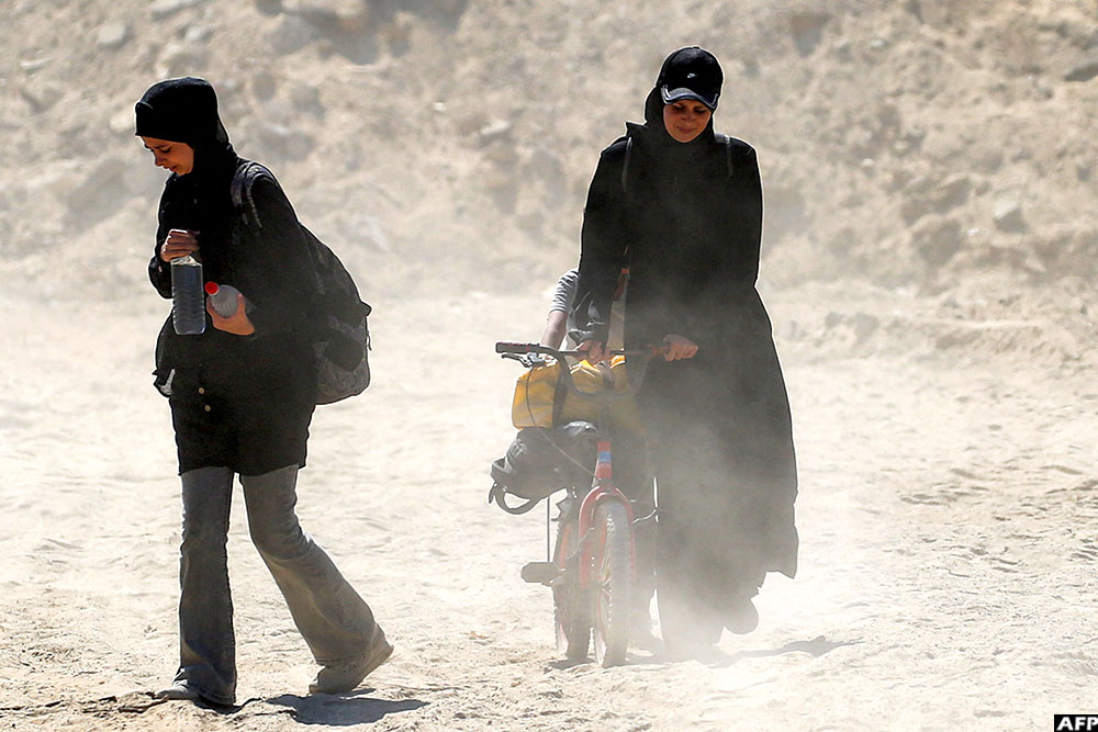 A woman walks with a child and a miniature bicycle through dust on the way to Gaza City through the so-called "Netzarim corridor" from Nuseirat in the central Gaza Strip on October 10, 2025
