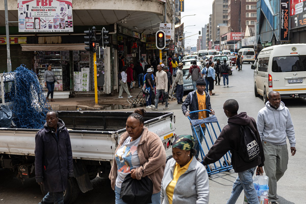 A worker pushes a trolley (3rd R) while walking through an intersection past other pedestrians in the Johannesburg CBD on November 7, 2025. 