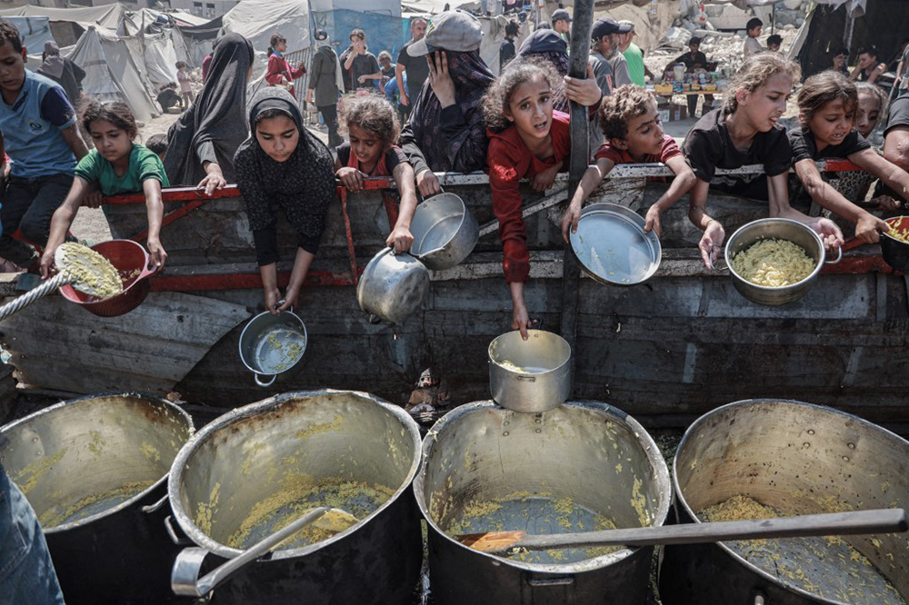 Palestinians, including children, try to receive hot meals, distributed by charity organizations, as people struggle to access food due to Israeli food blockade in Gaza City, Gaza on August 30, 2025. (Photo by Abdalhkem Abu Riash / Anadolu via AFP)