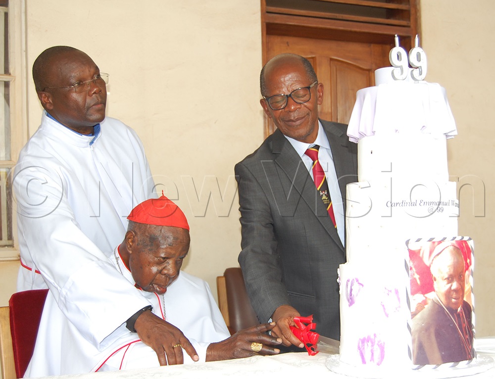 Cardinal Emmanuel Wamala (wearing a skull-cap) is joined by Hon. Dr John Chrysostom Muyingo (right) and his caretaker, Bro. Leonard Ssekiranda (left) as he cuts his 99th birthday cake. This was during the party organised by his extended family members at his retirement residence in Nsmbya, Makindye Division, on Saturday, December 27, 2025. (Photo by Mathias Mazinga)