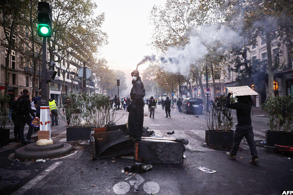 A protestor holds a smoke flare at the Boulevard des Capucines during a demonstration in Paris on October 17, 2026