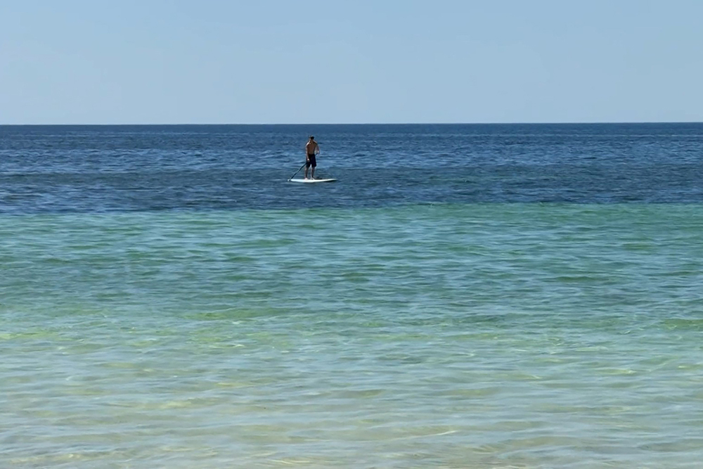 This frame grab from video footage from the Australian Broadcasting Corporation (ABC) taken on February 2, 2026 and received via AFPTV on February 3 shows a standup paddleboarder off the beach in Quindalup, Western Australia, with a view of the ocean where Austin Appelbee, 13, swam for four hours through choppy waters to get help for his family. (AFP)