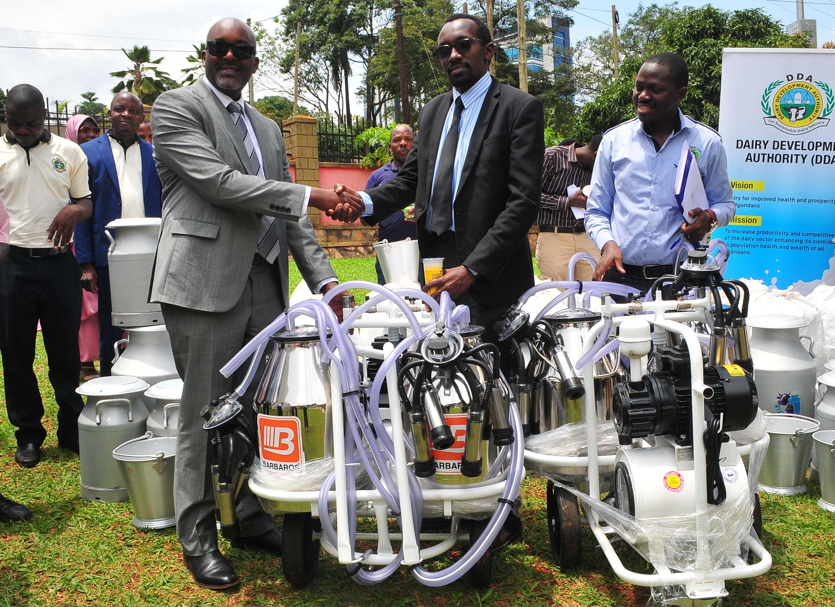 Samson Akankiza (left) the Acting Executive Director of Dairy Development Authority shakes hands with Frank Assimwe from Shemeza Farm at a handover ceremony of Milking equipment. (Photo by Nicholas Oneal)