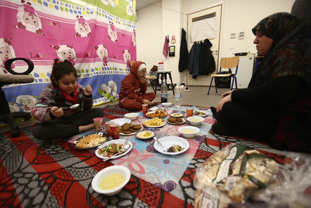 A displaced woman who lives with her family in a school's classroom after fleeing Israeli airstrikes in Beirut's southern suburbs, sit to break their fast together for the "iftar" meal in Beirut on March 7, 2026. (Photo by Ibrahim AMRO / AFP)