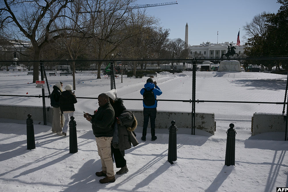 Tourists take pictures of the White House behind a security fence on January 27, 2026