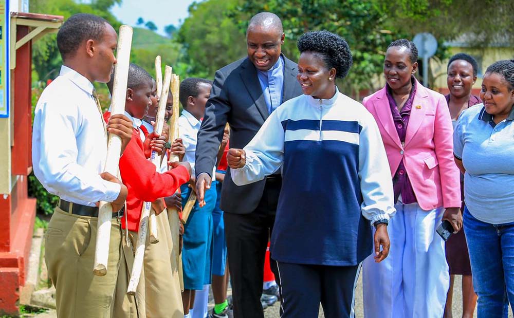 Rev. Robinson Balinda Stevenson, the Headteacher Nyakasura School, and students welcome Commissioner Hellen Seku, Acam Belinda, the Data Officer, Secretariat, National Secretariat for Patriotism Clubs (NSPC), State House, and Phiona Kobusingye, the Principal Officer NSPC for the function.