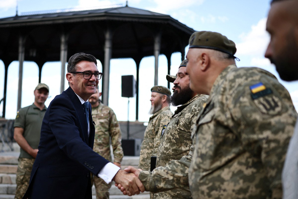 Britain's Prime Minister Andy Burnham (L) meets members of the military and artistic unit who perform on the front lines, in hospitals, and at rehabilitation centres, Cultural Forces Frontline, and the members of their mobile recording studio, in a park near Mykhailivska Square in Kyiv, on August 24, 2026, during his first trip abroad since taking office. (Photo by Henry NICHOLLS / POOL / AFP)
