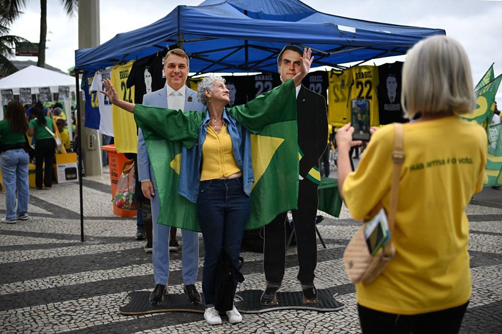 A supporter of Brazil's right-wing presidential candidate and senator Flavio Bolsonaro poses for a snapshot with life-size images of Flavio (L) and his father and former president (2029-2023) Jair Bolsonaro -now serving house arrest for an attempted coup d'etat- during a campaign rally at Copacaban beach in Rio de Janeiro, Brazil, on August 16, 2026.