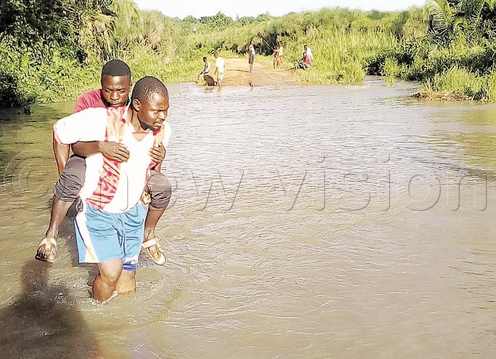 A man carrying a passenger through Kibalagala stream in Nabbaale sub-county, Mukono district. The Government said efforts are underway to improve road infrastructure development.