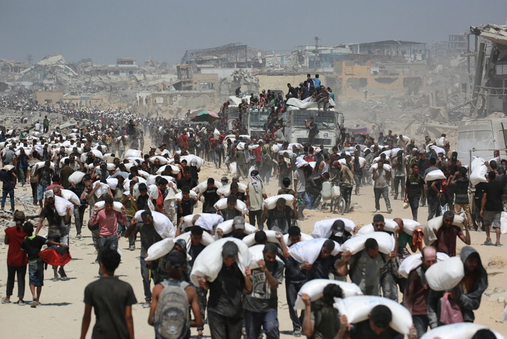 Palestinian walk carrying sacks of flour near Jabalia, in the northern Gaza Strip, on July 27, 2025, after trucks carrying humanitarian aid entered into northern Gaza coming from the Zikim border crossing. (Photo by BASHAR TALEB / AFP)