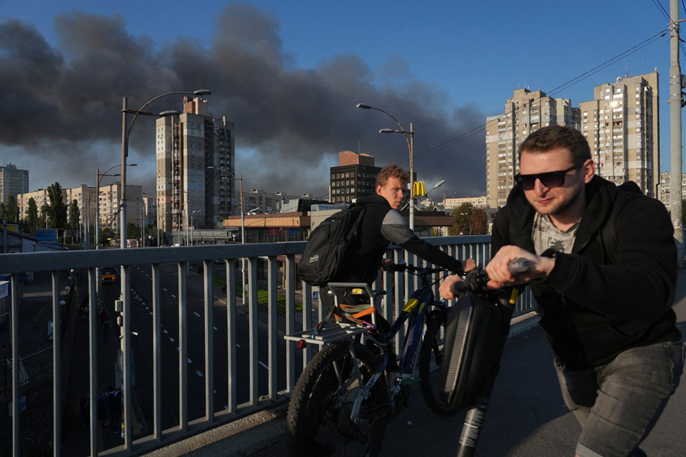 Local residents walk across a bridge as smoke rises following Russian drone and missile strike in Kyiv on September 7, 2025, amid the Russian invasion of Ukraine. (Photo by OLEKSII FILIPPOV / AFP)