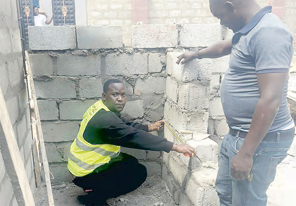 Ssebuufu (left) crouched beside the half-built wall, measuring the size of the bricks used. He is now setting his eyes on joining politics.