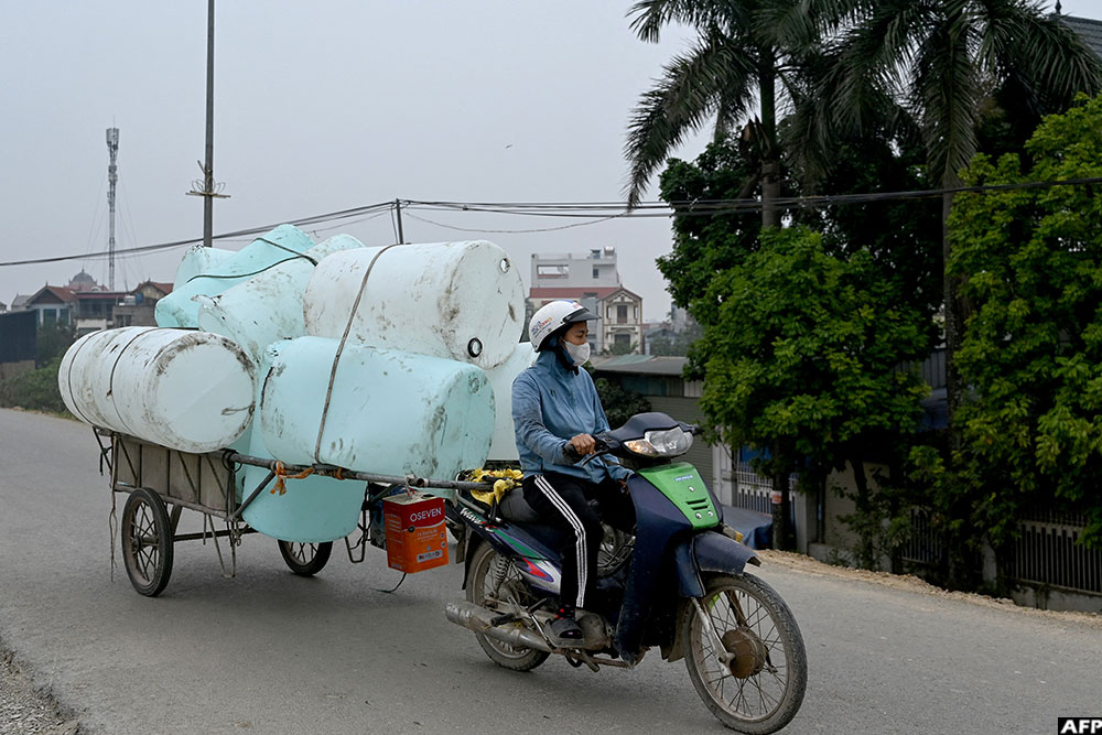 A woman rides a motorbike pulling a cart carrying plastic waste on a road on the outskirts of Hanoi, Vietnam