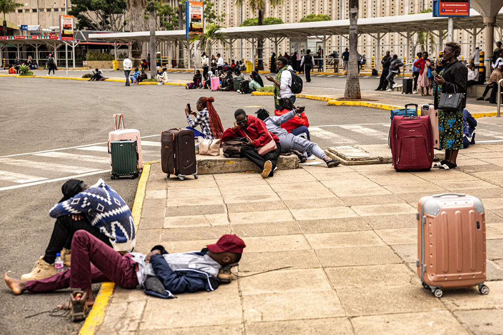 Stranded passengers sit on the pavement as they wait with their luggage by the departure terminal of the Jomo Kenyatta International Airport (JKIA) after staff from the Kenya Airports Authority (KAA) and Kenya Civil Aviation Authority (KCAA) airport workers' go-slow strike action continued into its second day, in Nairobi, on August 31, 2026.