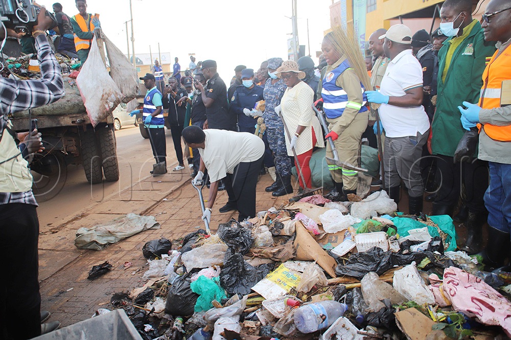 Prime Minister Robinah Nabbanja using a shovel to scoop rubbish before she dumps it on the waiting rubbish truck. Looking are other leaders from the area. (Photo by Peter Abaanabasazi)