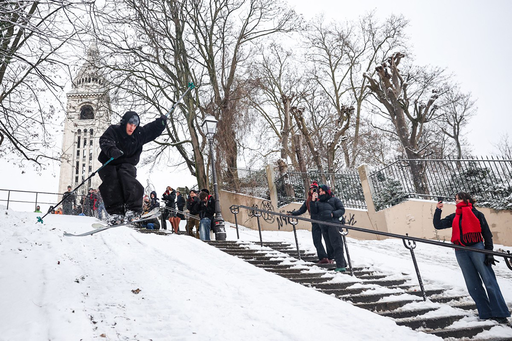 A skier jumps down a snow-covered slope next to spectating pedestrians at Montmartre following snowfalls in Paris, on January 7, 2026. (AFP)