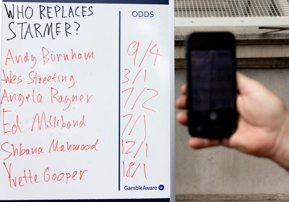 People take photographs of a betting company's odds on contenders to be the next leader of Britain's Labour party, with Andy Burnham, Wes Streeting and Angela Rayner's names all listed, on Whitehall in central London on May 12, 2026. (Credit: AFP)