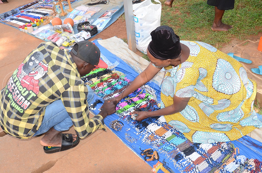 Maria Namugenyi, a religious item vendor selling to a customer at Namugongo Catholic Shrine during the scientific prayer celebrations on Wednesday, June 3, 2026, at Namugongo in Wakiso district. (Photo by Isaac Nuwagaba)
