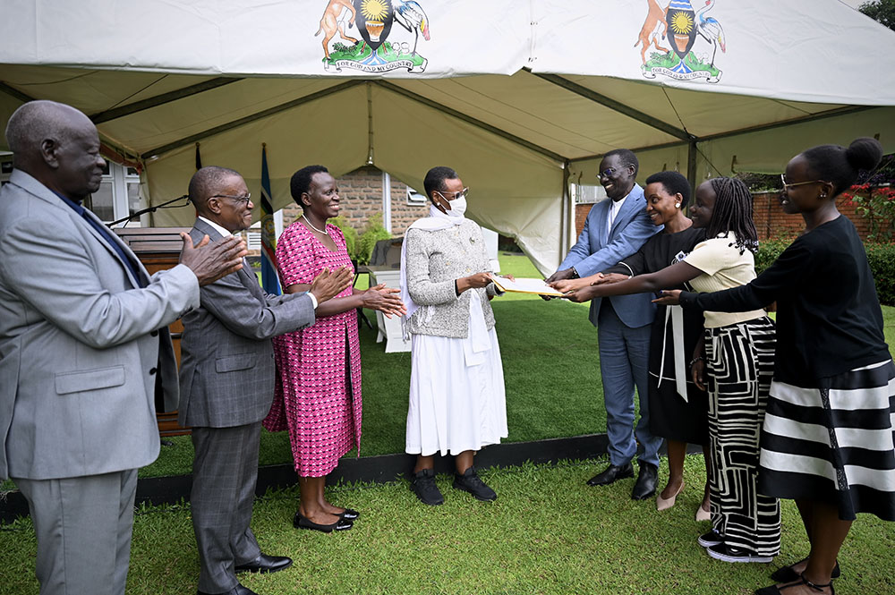 First Lady and Minister of Education and Sports, Hon. Janet K. Museveni, receives the land titles for the 97-acres for Bunyoro University from Dr. Henry Wamani and family, as officials and leaders applaud. (Credit: PPU)