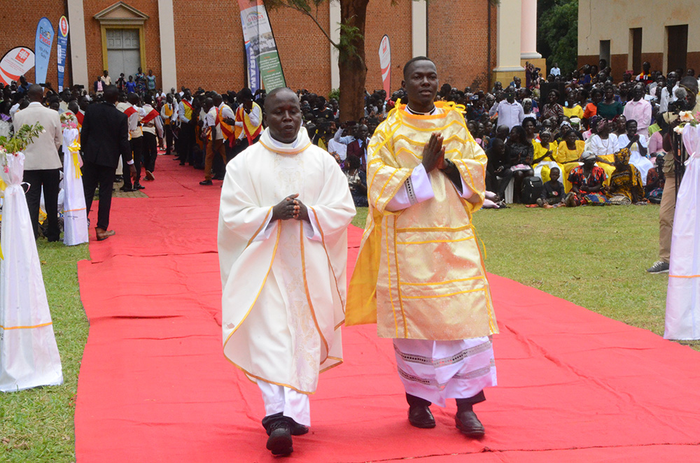 Newly ordained deacon Daniel Comboni Torach (R) escorted by his parish priest to the holy alter during the mass in Gulu City. (Photo by Johnisani Ocakacon)