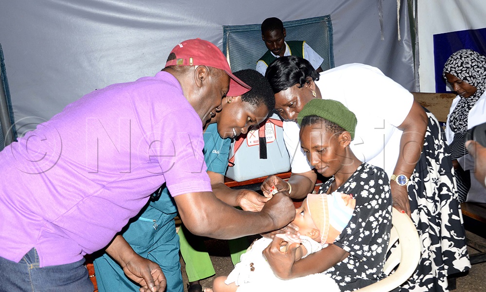 Chelangat Abigail, a midwife helps Robert Kavuma, president of Rotary Club of Kisugu Victoria to give a child polio drops as her mother looks on during the vaccination exercise at Kisugu Health Centre III at Namuwongo. (Photo by Juliet Kasirye)