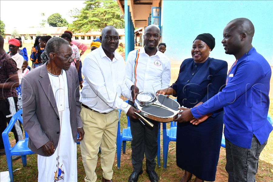 The Director General of Busoga Consortium for Development Anthony Mula (C) joined by Busoga Kingdom's State Minister of Education Nasabu Nantale (2nd R) handing over a height and weighing scale to Steven Makubo (2nd L), the headmaster of Buteme Light SDA Primary School while at Busana village in Kamuli district. (Credit: Donald Kiirya)