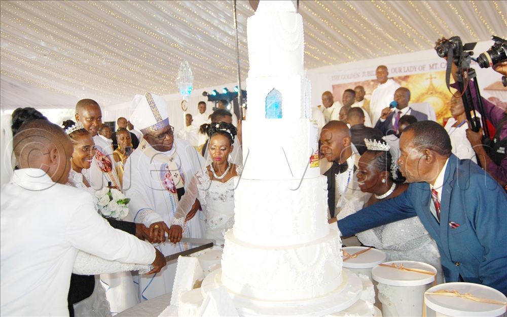 Archbishop Paul Ssemogerere (wearing a mitre) cuts cake with the couples that he wed during the grand celebration of the 50th anniversary of Our Lady of Mount Carmel Catholic parish Busega at the church in Rubaga Division on Sunday, July 12, 2026. 
