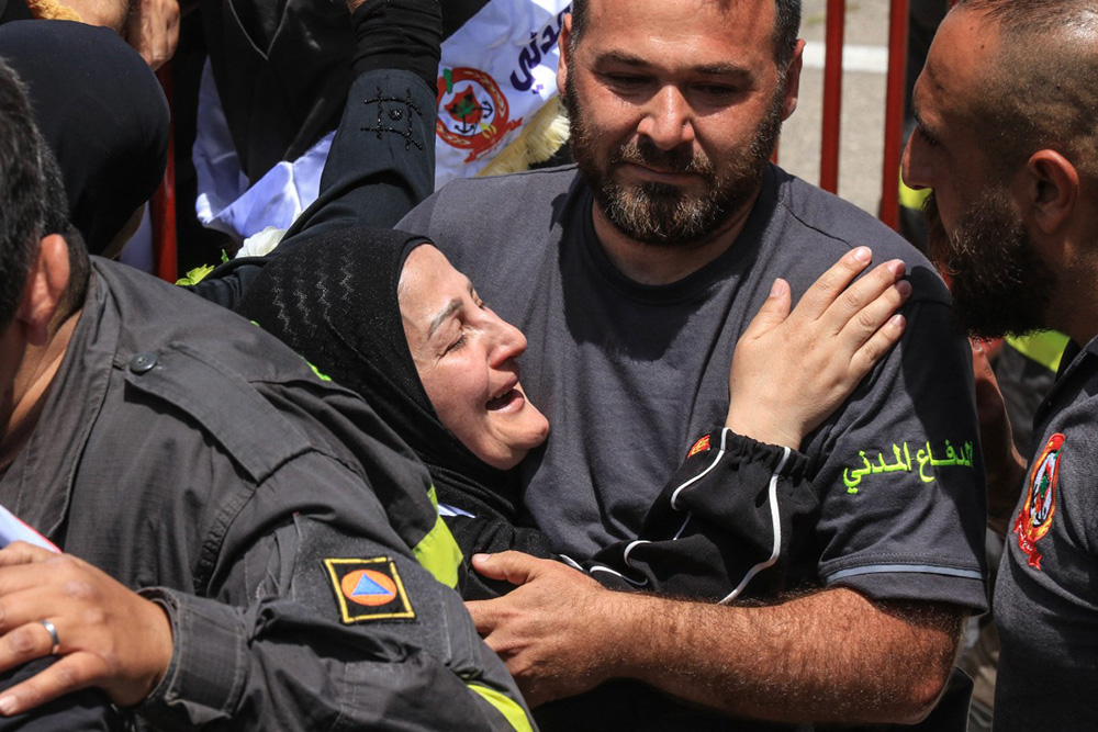 Fellow rescuers comfort a woman during the funerals of two civil defence members who were reportedly killed in Israeli airstrikes in Nabatieh the previous day, in the southern city of Sidon on May 13, 2026. (Photo by Mahmoud ZAYYAT / AFP)