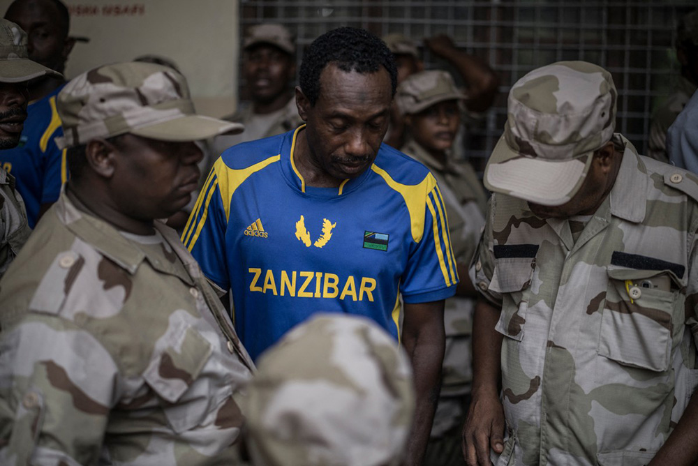 A voter wearing a Zanzibar football team jersey stands among members of various branches of Tanzania’s security forces queuing at a polling station in Stone Town on October 28, 2025, during early voting ahead of the October 29 general election. (Credit: AFP)