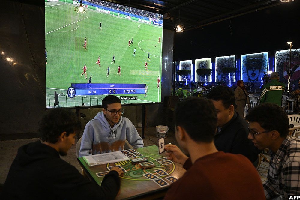 People play cards in a coffee shop in Egypt's capital Cairo on December 9, 2025, as the UEFA Champions League football match between Inter Milan and Liverpool is shown on a big screen. (AFP)