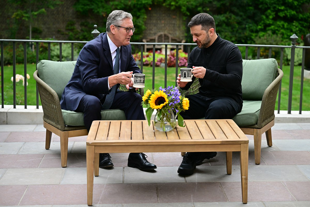 Britain's Prime Minister Keir Starmer (L) and Ukraine's President Volodymyr Zelensky hold mugs as they sit and talk in the garden of 10 Downing Street in central London, on August 14, 2025. 