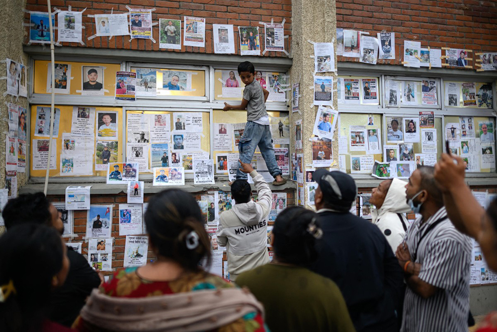 A young boy (C) climbs on a ledge to paste photographs of missing persons in the aftermath of flash floods, at the Tribhuvan University Teaching hospital in Kathmandu on August 31, 2026.