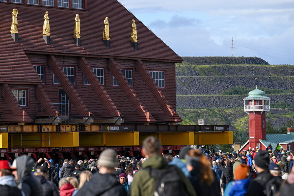 Peope gather to watch the moving of the wooden Kiruna Church, in Kiruna, Sweden on August 19, 2025. The church is being moved five kilometers to the new center of Kiruna due to the expansion of the iron ore mine operated by state-owned Swedish mining company LKAB. (Photo by Jonathan Nackstrand / AFP)